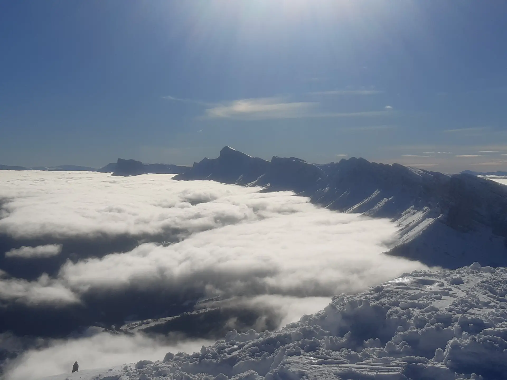Mer de nuages au pied d'une ligne de crêtes, sous un ciel bleu